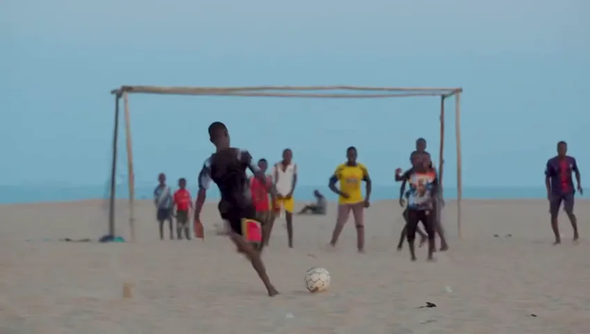 A line of players on a beach pitch in front of a goal of driftwood, the sea behind them